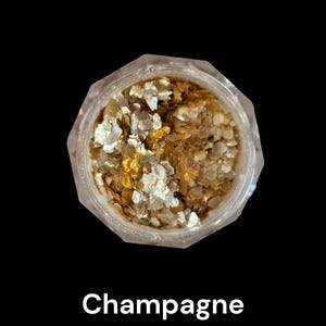 May include: A clear, faceted jar filled with shimmering gold and silver flakes. The jar is centered against a black background, with the word "Champagne" in white text below.