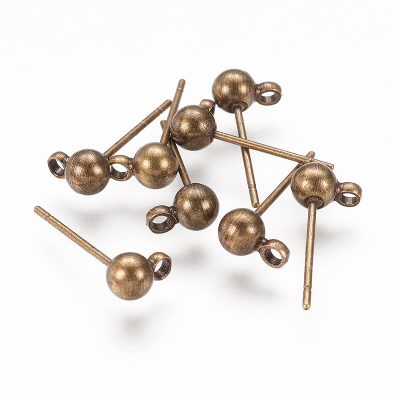 May include: A selection of antique bronze-toned earring posts. Each post has a small, spherical ball at the front with a loop and a straight post for insertion. The earrings are scattered on a white background.