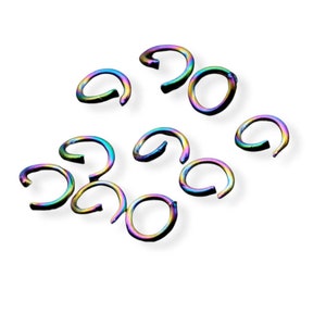 May include: A collection of iridescent metal spiral rings, each with a unique curved shape. The rings display a spectrum of colors, including blues, greens, and purples, against a white background. These decorative rings are likely used for jewelry making or crafting.