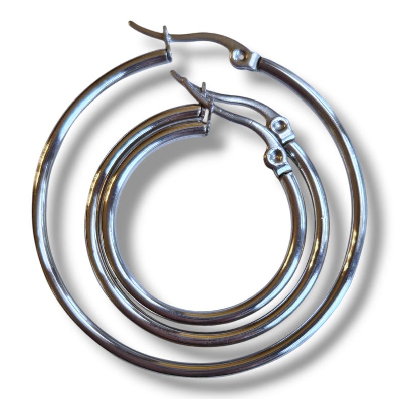 Peut inclure: Trois boucles d'oreilles cr&eacute;oles argent&eacute;es de tailles diff&eacute;rentes sont pr&eacute;sent&eacute;es. Les boucles d'oreilles sont en m&eacute;tal brillant et ont un design circulaire classique. Les cr&eacute;oles sont reli&eacute;es par un fermoir &agrave; charni&egrave;re. Les boucles d'oreilles sont pr&eacute;sent&eacute;es sur fond blanc.
