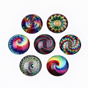May include: Seven round glass cabochons with colorful, swirling designs. The cabochons feature a variety of patterns, including tie-dye, spirals, and geometric shapes in shades of red, blue, green, yellow, and purple. The cabochons are arranged on a white background.