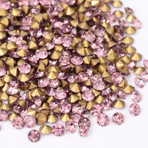 May include: A collection of pink and gold rhinestones. The pink rhinestones are round with a faceted surface, while the gold rhinestones are pyramid-shaped. These decorative embellishments are ideal for crafts and jewelry making.