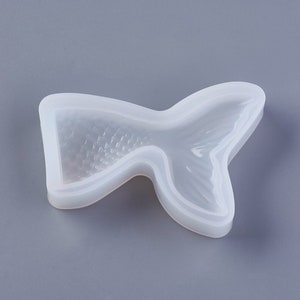 May include: A clear, flexible silicone mold in the shape of a mermaid tail. The mold features detailed scales and fin patterns. The tail curves gracefully, perfect for crafting projects. The mold is designed for creating resin or other craft items.