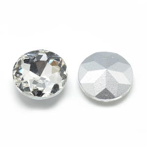 May include: Two round, faceted rhinestones. One is clear and sparkling, the other is silver and opaque. The rhinestones are set against a white background. These decorative embellishments are suitable for crafts and jewelry making.