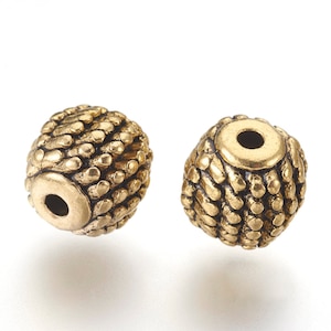 May include: Two antique gold-colored beads with a textured surface. Each bead has a cylindrical hole through the center. The beads have an oval shape and a detailed, bumpy texture, creating a vintage aesthetic.