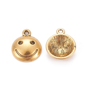 May include: Two antique gold-colored smiley face charms. Each charm is round with a loop at the top for stringing. One charm features a smiling face, while the other has a textured back.