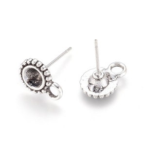 May include: Two silver-colored earring posts with a round, beaded bezel and a small loop. The posts are designed for jewelry making. One earring post is face up, and the other is face down.