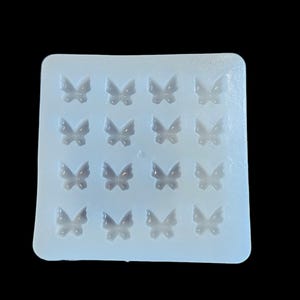 May include: A clear, rectangular silicone mold with 16 butterfly-shaped cavities. The mold is designed for crafting small, decorative butterfly elements. The butterflies are evenly spaced and detailed.