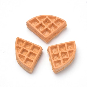 May include: Three miniature, light brown waffles with a square grid pattern are arranged on a white background. The waffles are cut into quarter and half sections, showcasing their detailed texture and shape. The image is well-lit, highlighting the details.