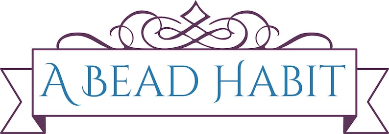 May include: A logo featuring the text "A BEAD HABIT" in a stylized font. The text is in blue, set against a white rectangular banner with a purple border and ribbon-like extensions. An ornate purple flourish tops the banner.