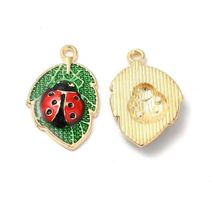 May include: Two gold-colored ladybug charms. One charm features a red and black ladybug on a green leaf with a gold outline. The other charm is a gold-colored leaf with a ladybug imprint. Both charms have a small loop at the top for attaching to jewelry.
