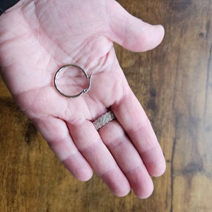 Peut inclure: Une boucle d'oreille argent&eacute;e avec une fermeture &agrave; charni&egrave;re. La boucle d'oreille est tenue dans une main ouverte, avec une bague au doigt. Le fond est une surface en bois.