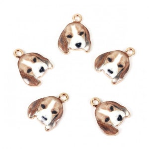 May include: Five gold-toned dog head charms with a beagle-like appearance. Each charm features a detailed painted face with brown, white, and black markings. The charms have a small loop at the top for attaching to jewelry or other crafts.