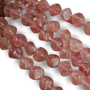 May include: Strands of pinkish-red, square-cut gemstone beads. The beads have a translucent quality, with variations in color and texture. The beads are strung together, ready for jewelry making or other craft projects.