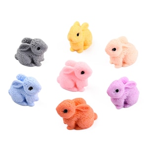 May include: Seven small, colorful bunny figurines in various pastel shades: gray, yellow, peach, blue, pink, orange, and purple. Each bunny has black eyes and is posed in a sitting position. The figurines are likely for crafts or decoration.