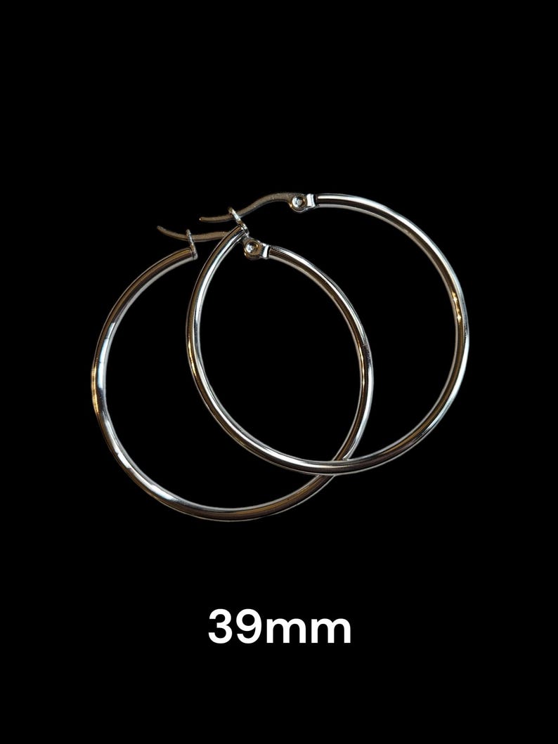 Peut inclure: Une paire de boucles d'oreilles cr&eacute;oles argent&eacute;es sur fond noir. Les boucles d'oreilles sont circulaires, avec un design simple et poli. Le texte "39mm" est affich&eacute; en dessous, indiquant leur taille, soit environ 3,9 cm.