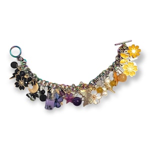 May include: A charm bracelet with a rainbow chain and a variety of charms. Charms include black flowers, a butterfly, a boba tea cup, purple stars, yellow flowers, and other decorative elements. The bracelet has a toggle clasp.