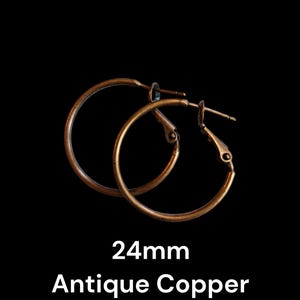 May include: A pair of antique copper hoop earrings, each 24mm in diameter, against a black background. The earrings have a warm, aged bronze color and a simple, classic design. The text "24mm Antique Copper" is displayed below the earrings.