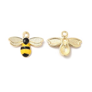 May include: Two bee-shaped charms. One charm is painted with yellow and black stripes on the body, black head, and gold wings. The other charm is gold with detailed wing patterns. Both charms have a small loop at the top for attaching to jewelry.