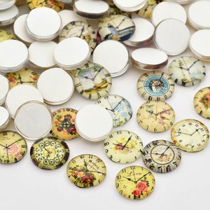 May include: A collection of round glass cabochons, some with blank white surfaces, others featuring vintage clock faces with floral and nautical designs. The clock faces display Roman numerals and decorative hands, with a variety of colors and styles.