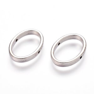 May include: Two oval-shaped, silver-colored metal rings with small holes. The rings are positioned side-by-side against a white background. The metal has a slightly brushed appearance.