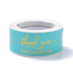 May include: A roll of teal stickers with gold lettering. The text reads "thank you" in a cursive font, with "FOR YOUR ORDER" below in a sans-serif font. The stickers are on a white background.