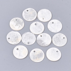 May include: A collection of round, off-white shell pendants with a pearlescent sheen. Each pendant has a small hole near the top for stringing. The pendants are arranged on a light gray surface.