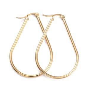 May include: A pair of gold-colored teardrop hoop earrings. The earrings have a slender, elongated design with a smooth, polished finish. The hoops are connected by a hinged clasp at the top.