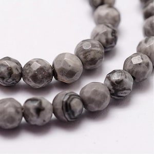 May include: Close-up of a strand of gray gemstone beads. The beads are faceted, with a mix of light and dark gray tones and subtle patterns. The beads are round and appear to be strung together.