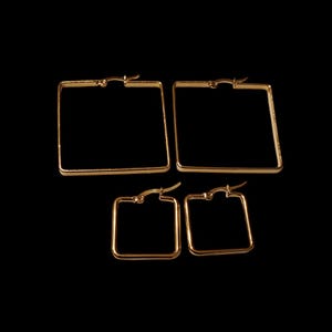 May include: Four gold-colored square hoop earrings of varying sizes are displayed against a black background. The earrings have a simple, geometric design, with a hinged closure. The earrings are likely made of metal and are suitable for everyday wear.