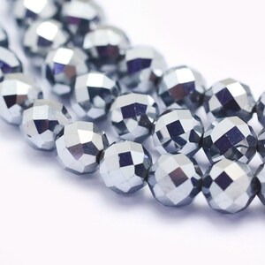 May include: Close-up of several strands of faceted, silver-colored beads. The beads have a geometric, multi-faceted design, reflecting light. The beads are strung together, suggesting they are for jewelry making or crafting.