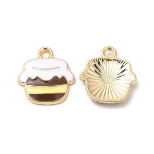 May include: Two gold-colored charms in the shape of a honey pot. One charm is enameled with white, brown, and yellow, while the other is a solid gold with a sunburst design. Both have a small loop at the top.