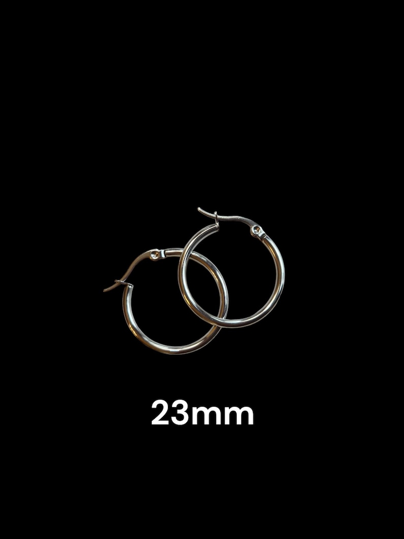 Peut inclure: Une paire de boucles d'oreilles cr&eacute;oles argent&eacute;es, chacune avec un design circulaire simple. Les boucles d'oreilles mesurent 2,3 cm de diam&egrave;tre et sont pr&eacute;sent&eacute;es sur fond noir. Le texte "23mm" est affich&eacute; en dessous.