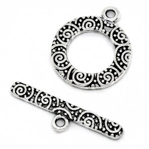 May include: A silver-toned toggle clasp set, featuring a circular ring and a bar. Both pieces are adorned with an intricate, swirling pattern. The clasp is designed for jewelry making and crafting.