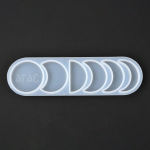 May include: A light blue silicone mold featuring a series of moon phases. The mold has a long, oval shape with a circular section and five crescent moon shapes. The text "ΔΓΔΕ" is visible in the circular section. The mold is designed for crafting.