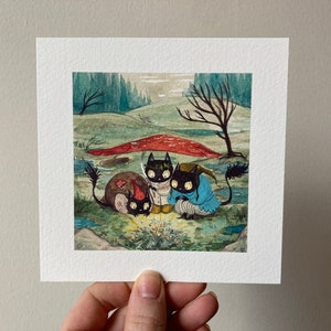 May include: A watercolour painting depicting three black cat-like figures in a fantastical forest setting. One wears a red hat, another a blue cloak, and the third a white outfit. A red mushroom and bare trees are in the background.