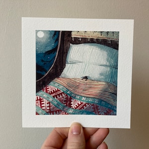 Può includere: Un dipinto ad acquerello raffigura una scena di camera da letto accogliente. Un letto con un cuscino a righe e una coperta fantasia è illuminato dalla luce della luna da una finestra rotonda. L'opera d'arte è tenuta in mano, mostrando i dettagli della stampa quadrata.