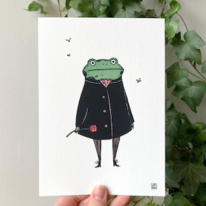 May include: A quirky illustration of a green frog in a black coat, holding a flower. The frog has a pink collar and is standing on black stockings and shoes. Two small insects are flying around the frog on a white background.