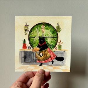 May include: Watercolor illustration of a black cat in a kitchen setting. The cat, wearing an apron and red scarf, carries a loaf of bread. A round window with green foliage and hanging herbs is in the background. A red vase and wooden spoons are on the counter.