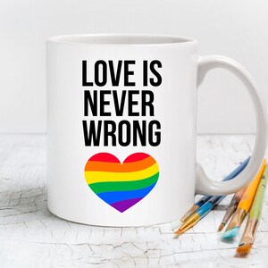 May include: White ceramic mug with the text "LOVE IS NEVER WRONG" in black lettering and a rainbow heart graphic.