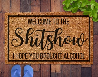 May include: A brown coir doormat with black text that reads "Welcome to the Shitshow I hope you brought alcohol".