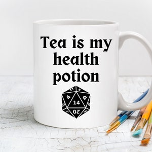 May include: White ceramic mug with a black graphic that reads "Tea is my health potion" and a black and white image of a twenty-sided die.
