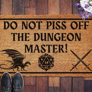 May include: A brown coir doormat with the text "Do Not Piss Off The Dungeon Master!" in black lettering. A black dragon with wings is on the left side of the mat. A black 20-sided die with the number 14 showing is on the right side of the mat. Two black swords are crossed in the upper right corner of the mat.