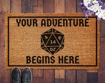 May include: A brown doormat with the text "Your adventure begins here" and a black and white 20-sided die in the center.