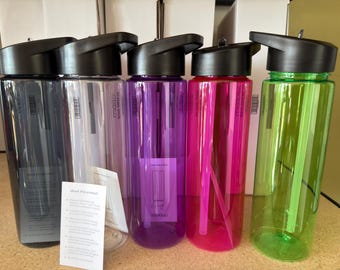 May include: A collection of clear plastic water bottles in various colors, including gray, purple, pink, and green. Each bottle has a black lid with a flip-top opening. The bottles are arranged in a row, showcasing their vibrant hues and sleek design.