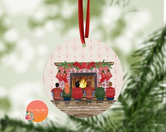 May include: A round Christmas ornament with a pink background and a fireplace scene. Six people are sitting in front of the fireplace wearing sweaters and hats. The names Ryan, Angel, Jay, Tony, Michael, and Eric are written below the people.