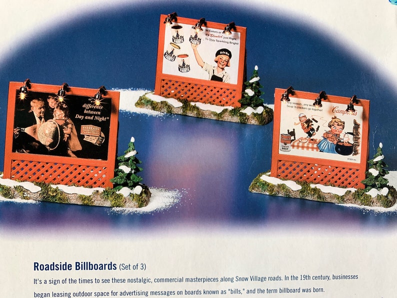 May include: A set of three miniature roadside billboards with vintage advertisements. The billboards are made of wood and have a red lattice design. The advertisements feature images of people and products from the past. The billboards are set on a snowy base with small evergreen trees.