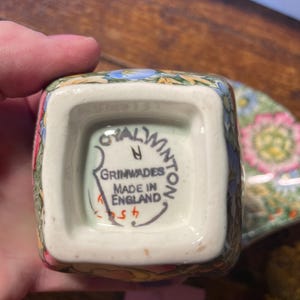 Może przedstawiać: Kwadratowy ceramiczny kubek w kwiaty z napisem "Royal Winton Grimwades Made in England" na spodzie. Kubek ma kolorowy wz&oacute;r z r&oacute;żowymi, niebieskimi i ż&oacute;łtymi kwiatami. Częściowo widoczny jest pasujący spodek.