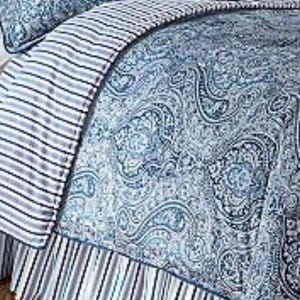 May include: A blue and white paisley patterned comforter with a striped border and bed skirt. The bedding features a detailed, ornate design in shades of blue and white, creating a classic and elegant look. The striped border adds a contrasting element.