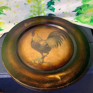 May include: Set of two brown wooden plates with a gold rim. Each plate features a painted image of a rooster with a yellow comb and wattle.